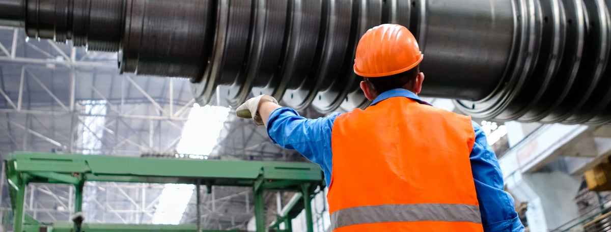 Factory worker in an orange hard hat, hi-vis vest and work gloves pointing at machinery